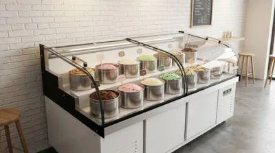 Large capacity commercial ice cream freezer in a bright dessert parlor, displaying multiple flavors of frozen desserts with easy-access glass sliding doors.