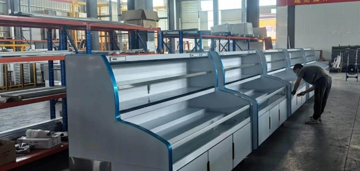 A factory worker performing quality inspection on a long row of commercial display freezers to ensure consistent production standards.