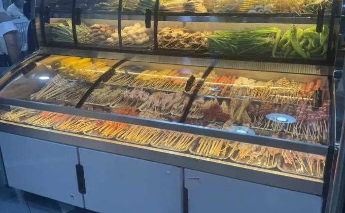 Multi-temperature food selection counter in a BBQ restaurant, organized with fresh skewers and vegetables for customer self-service.