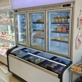 Brightly lit self-service combi freezer in a bakery cafe, showcasing pastries and chilled desserts to customers.